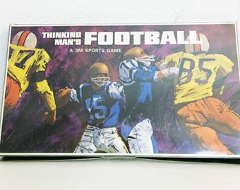 May include: A vintage board game box with a colorful illustration of football players. The box is titled "Thinking Man's Football, A 3M Sports Game".