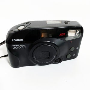 May include: A black Canon Sure Shot Zoom-S camera with a built-in flash and a lens that reads "Canon Zoom Lens 38-80mm 1:3.5-8.5".