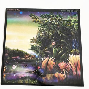 May include: A vinyl record album cover featuring a jungle scene with lush green foliage, a river, and a white bird. The album title "Tango in the Night" and the artist "Fleetwood Mac" are printed in white text on a black background.