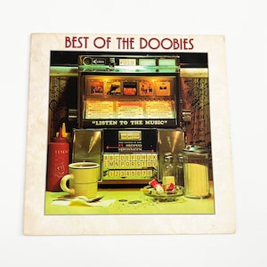 May include: A vintage record album cover featuring a retro diner scene with a jukebox playing "Listen to the Music" and a cup of coffee on a table with salt and pepper shakers. The album cover is for "Best of the Doobie Brothers".