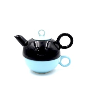 May include: A two-tone ceramic teapot with a matching teacup. The top half of the teapot is black, while the bottom half and teacup are light blue. The teapot has a black handle and spout, and a light blue lid with a small handle.