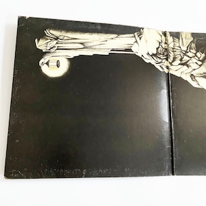 May include: A black and white vinyl record album cover with a large, shadowy figure holding a lantern. The figure is standing on a rocky cliff, and the background is a dark, stormy sky.
