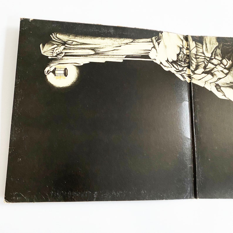 May include: A black and white vinyl record album cover with a large, shadowy figure holding a lantern. The figure is standing on a rocky cliff, and the background is a dark, stormy sky.