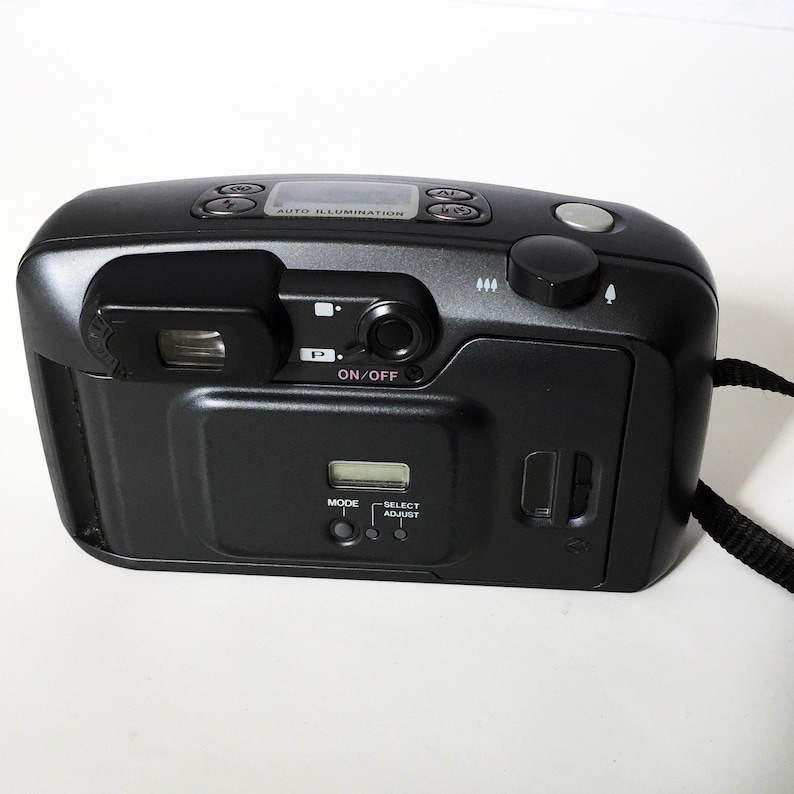 The back of a dark gray Pentax IQZoom 140 35mm film camera is shown, featuring the viewfinder, an LCD screen, and control buttons.