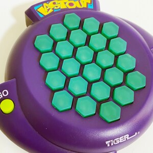 May include: Purple handheld electronic game with the word "Last One" on the top and the word "Tiger" on the bottom. The game has a green honeycomb pattern with 25 buttons.