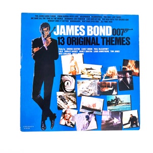 May include: A blue and white record album cover featuring James Bond 007 with 13 original themes. The cover features a collage of images from the James Bond films, including scenes from "From Russia with Love", "Goldfinger", "Thunderball", "You Only Live Twice", "Diamonds Are Forever", "Live and Let Die", "The Man with the Golden Gun", "Nobody Does It Better", "Moonraker", "For Your Eyes Only", and "All Time High".