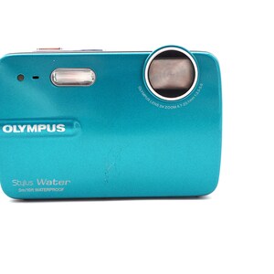 May include: A teal Olympus Stylus Water 3m/10ft waterproof digital camera with a black strap.