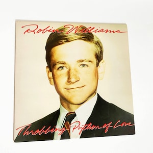 May include: A vintage record album cover featuring a young Robin Williams with the album title "Throbbin' Python of Love" in red lettering.