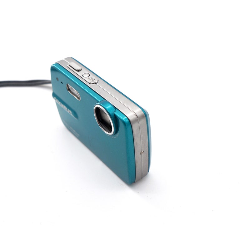 May include: A teal and silver digital camera with a lens cover and a strap.