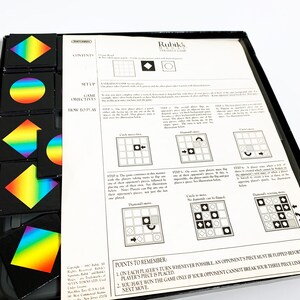 May include: A game board with a grid pattern and colorful pieces with diamond, circle, and square shapes. The game is called Rubik's Strategy Game and includes instructions on how to play.