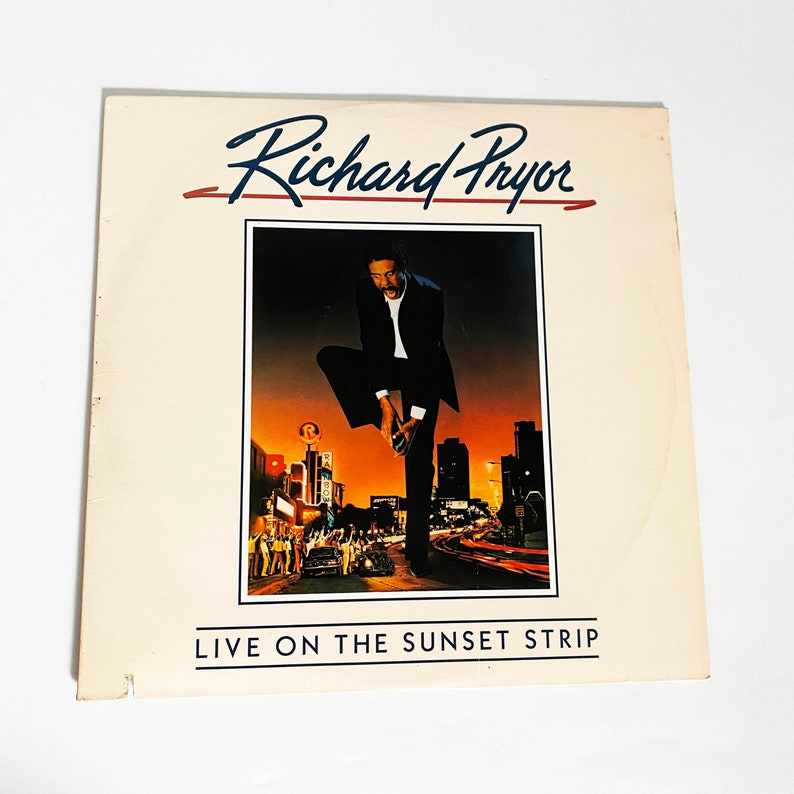 Puede incluir: Una portada de &aacute;lbum de vinilo vintage con el comediante Richard Pryor. El arte de la portada muestra a Pryor de pie en una calle de la ciudad, con un paisaje urbano en el fondo. El t&iacute;tulo del &aacute;lbum, "Live on the Sunset Strip", est&aacute; impreso en letras blancas en la parte inferior de la portada.