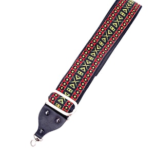 May include: A black and patterned guitar strap with a colorful design. The strap features a woven pattern in red, green, and yellow against a black background. It has a metal buckle and leather ends.