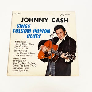May include: A vintage vinyl record cover featuring Johnny Cash, a country music legend, with the title "Johnny Cash Sings Folsom Prison Blues". The cover features a black and white photo of Cash playing a guitar, with the album title in blue and white text.