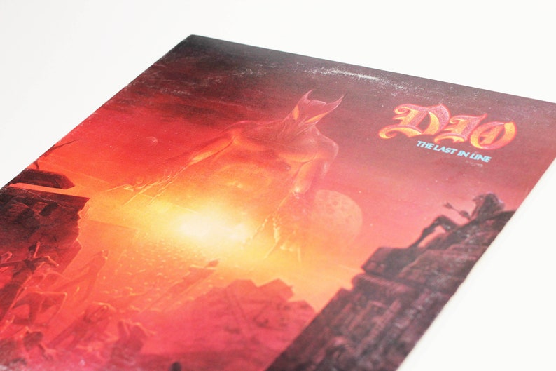May include: A red and orange album cover with a large, shadowy figure in the center. The album title "DIO" and the subtitle "The Last in Line" are printed in white at the top of the cover.