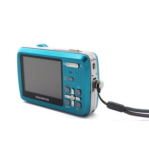 May include: A teal blue digital camera with a black strap. The camera has a screen, buttons, and the word "OLYMPUS" printed on the front.