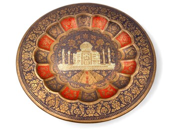 May include: Ornate, round, decorative plate with a gold, red, and navy blue color scheme. The plate features a detailed floral pattern around the edge and a central image of a building with multiple spires.