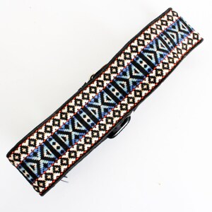 May include: A black guitar strap with a colorful geometric pattern in shades of blue, orange, and white.