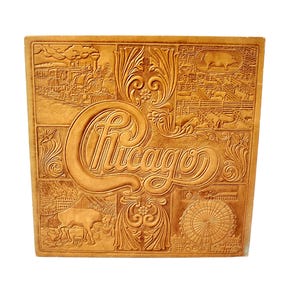 May include: A tan leather square with the word "Chicago" embossed in a stylized font. The design includes images of a train, Ferris wheel, and livestock, with decorative floral elements.