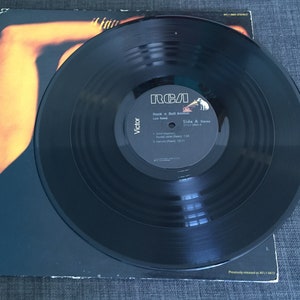 May include: A black vinyl record with a white label. The label has the text "RCA" in red, "Rock 'n' Roll Animal" in black, "Lou Reed" in black, "Side A:  Street Hassle" in black, "Victor" in black, and a list of songs with their lengths in black.