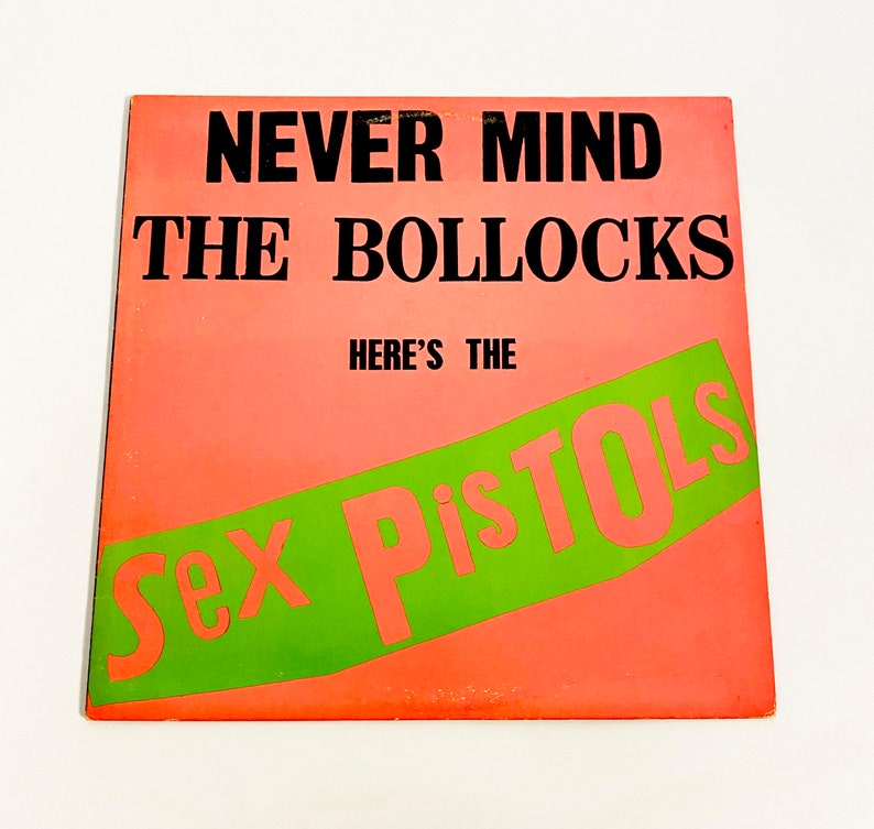 May include: A pink and green vinyl record album cover with the text "Never Mind The Bollocks Here's The Sex Pistols".