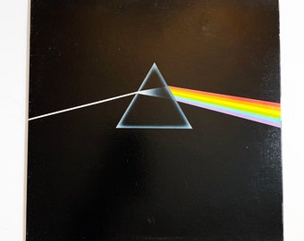 Puede incluir: Una portada de álbum de vinilo negra con un prisma triangular y un haz de luz blanca que se convierte en arcoíris. El diseño es minimalista y destaca los colores vibrantes del espectro.