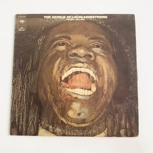 May include: A vintage vinyl record album cover featuring a close-up portrait of Louis Armstrong with his mouth open in a loud, exaggerated expression. The album title "The Genius of Louis Armstrong, Volume 1, 1925-1932" is printed in white on a brown background.