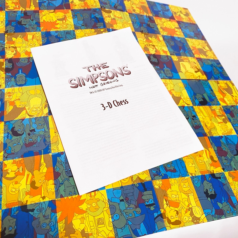 May include: A white board game box with a checkered pattern on the front and back. The box has a title that reads "The Simpsons Matt Groening TM & &copy; 1990 20th Century Fox Film Corp. 3-D Chess".