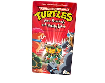 May include: A red VHS tape for the Teenage Mutant Ninja Turtles cartoon, titled "Super Rocksteady und Mighty Bebop." The cover features cartoon characters and the text "For Ages 5 and Up."