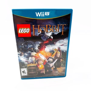 May include: A blue Nintendo Wii U game case with a Lego The Hobbit video game cover. The cover features a red dragon, a group of Lego characters, and the game title in white text.
