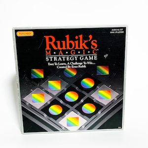 May include: A black and silver game board with a rainbow colored design. The game is called "Rubik's Magic" and is a strategy game for two players. The game is created by Erno Rubik.