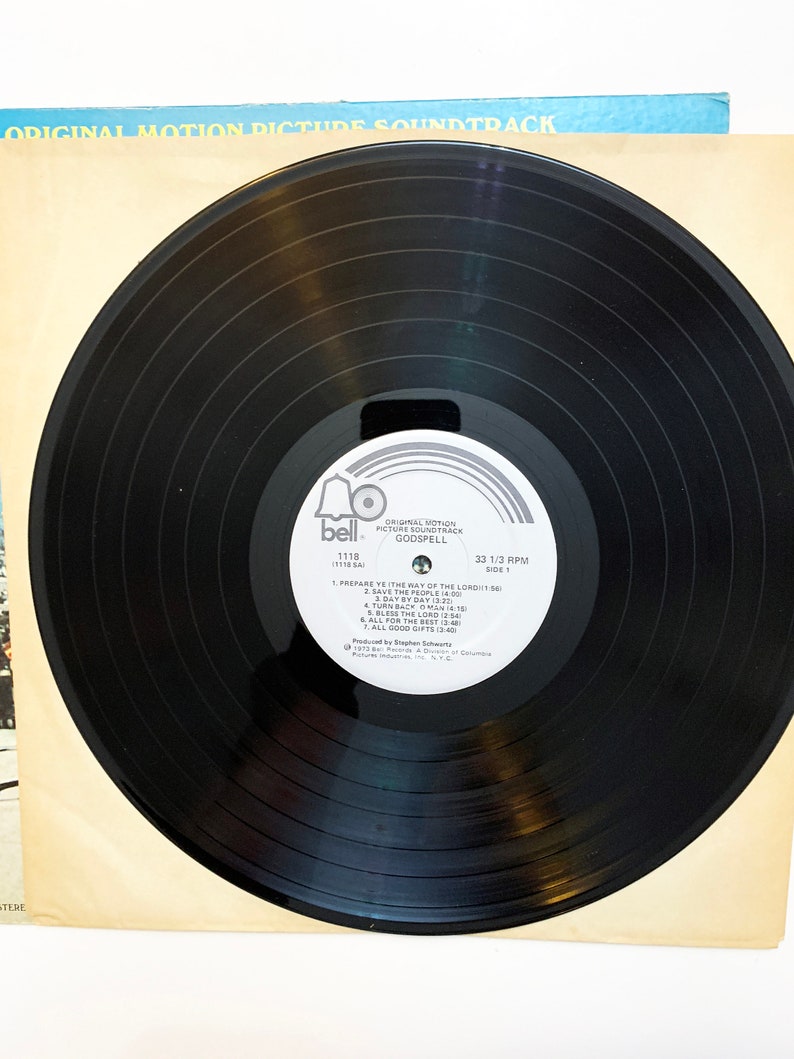 May include: Black vinyl record with a white label. The label has a bell icon and the text "Original Motion Picture Soundtrack Godspell 1118 (THSA) 33 1/3 RPM Side 1". The track list includes "Prepare Ye The Way Of The Lord", "Save The People", "Day By Day", "Turn Back O Man", "Bless The Lord", "All For The Best", and "All Good Gifts".