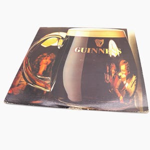 May include: A vintage vinyl record album cover featuring a large glass of Guinness beer with the Guinness logo and a group of people in the background.