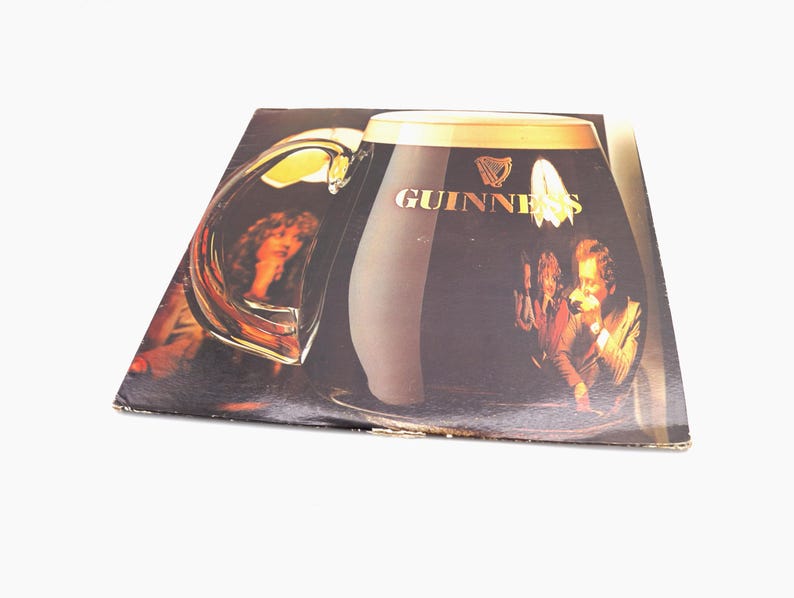 May include: A vintage vinyl record album cover featuring a large glass of Guinness beer with the Guinness logo and a group of people in the background.