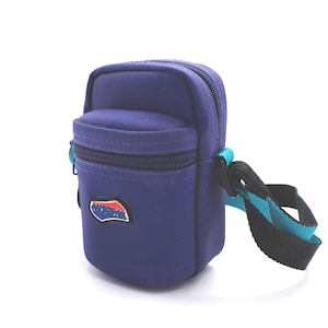 May include: A small purple crossbody bag with a blue and red logo. The bag has a zippered pocket on the front and a black strap with a turquoise stripe.