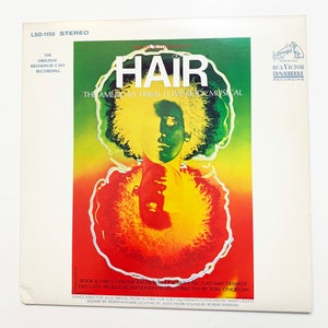 May include: A vintage vinyl record cover for the original Broadway cast recording of the musical "Hair: The American Tribal Love-Rock Musical". The cover features a psychedelic design with a close-up of a person's face with long, curly hair.