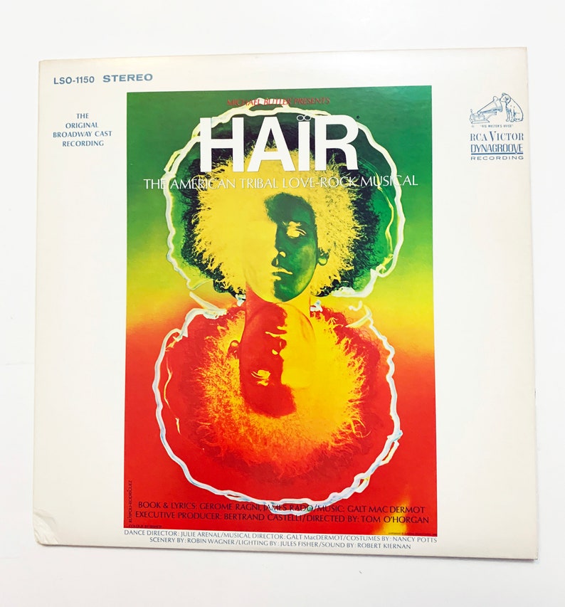 May include: A vintage vinyl record cover for the original Broadway cast recording of the musical "Hair: The American Tribal Love-Rock Musical". The cover features a psychedelic design with a close-up of a person's face with long, curly hair.