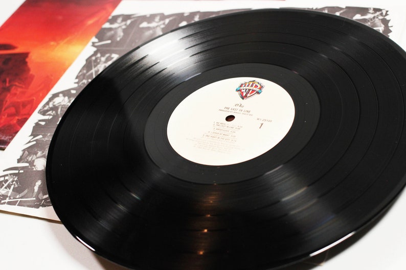 May include: A black vinyl record with a white label. The label has the text "The Last In Line" and the artist's name "Ozzy" printed on it. The record is part of a vinyl record collection.