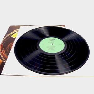May include: A black vinyl record with a green label. The label has the text "Columbia" and "The Rolling Stones" in white. The record is on a white surface.