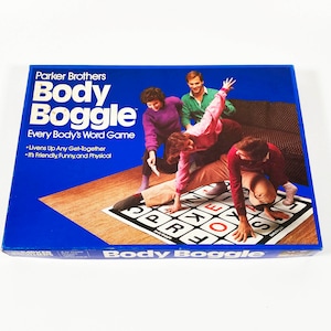 May include: A blue box with the words "Parker Brothers Body Boggle Every Body's Word Game" on the front. The box shows four people playing the game, which involves a board with letter tiles. The game is described as "Livens Up Any Get-Together" and "It's Friendly, Funny, and Physical."