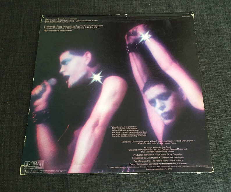 May include: A black and white vinyl record album cover featuring two people in black clothing with white makeup. The album title is "White Light/White Heat/Lady Day/Rock 'n' Roll" by Lou Reed. The back cover includes the song titles, musicians, and production information.
