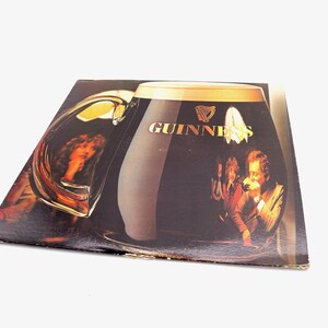 May include: A vintage vinyl record album cover featuring a large glass of Guinness beer with the Guinness logo and a group of people enjoying the beer.