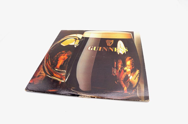 May include: A vintage vinyl record album cover featuring a large glass of Guinness beer with the Guinness logo and a group of people enjoying the beer.