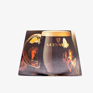 May include: A vintage vinyl record album cover featuring a large glass of Guinness beer with a woman's face reflected in the glass. The album cover is brown and black with the Guinness logo and text.