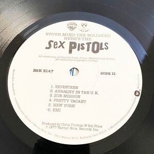 May include: Black and white vinyl record with a white label. The label has the text "Never Mind The Bollocks Here's The Sex Pistols" and the track list for side two of the record. The track list includes "Seventeen", "Anarchy In The U.K.", "Sub-Mission", "Pretty Vacant", "New York", and "EMI".