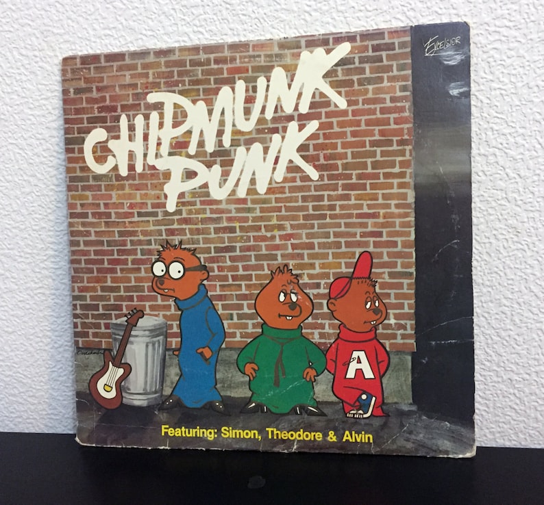 May include: A vintage record album cover featuring the cartoon characters Alvin, Simon, and Theodore from the Alvin and the Chipmunks franchise. The album cover is titled "Chipmunk Punk" and features the three chipmunks dressed in punk rock attire. The album cover is set against a brick wall background.