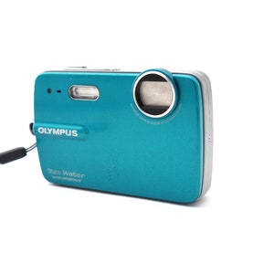 May include: A teal blue Olympus Stylus Water digital camera with a silver lens ring and a black wrist strap. The camera has the text "Olympus" and "Stylus Water" printed on the front.