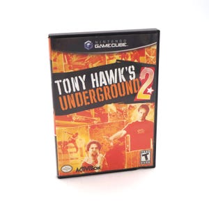 May include: A black Nintendo GameCube game case for "Tony Hawk's Underground 2." The cover features the game title in orange and white, with images of skateboarders and the Activision logo. The case is in a vertical orientation.