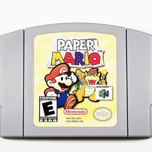 May include: A silver Nintendo 64 game cartridge for Paper Mario. The front of the cartridge features a colorful illustration of Mario and a Koopa. The game is rated E for Everyone by the ESRB.
