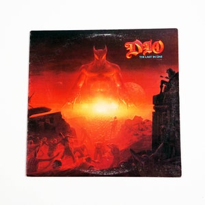 May include: A vinyl record cover featuring a red, demonic figure with horns and a glowing red background. The text "DIO" and "THE LAST IN LINE" is printed in white on the cover.