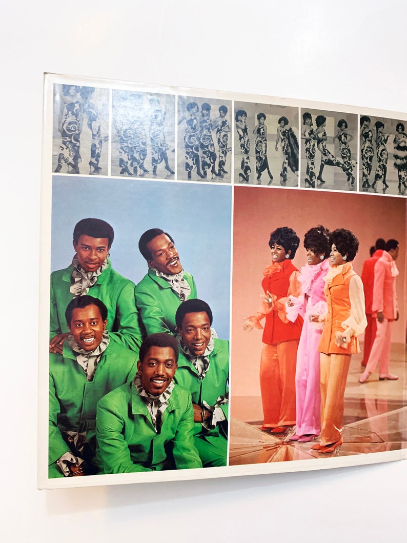 May include: A vintage record album cover featuring a group of six people, four men and two women, dressed in colourful 1970s clothing. The men are wearing green suits with white collars, and the women are wearing pink, orange and red dresses. The album cover has a blue and white background.